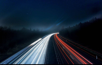 En motorvei om natten midt i skogen med lysstråler som representerer kjøretøyenes hastighet.