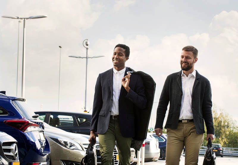Two elegantly dressed and smiling gentlemen casually walking over a parking lot.