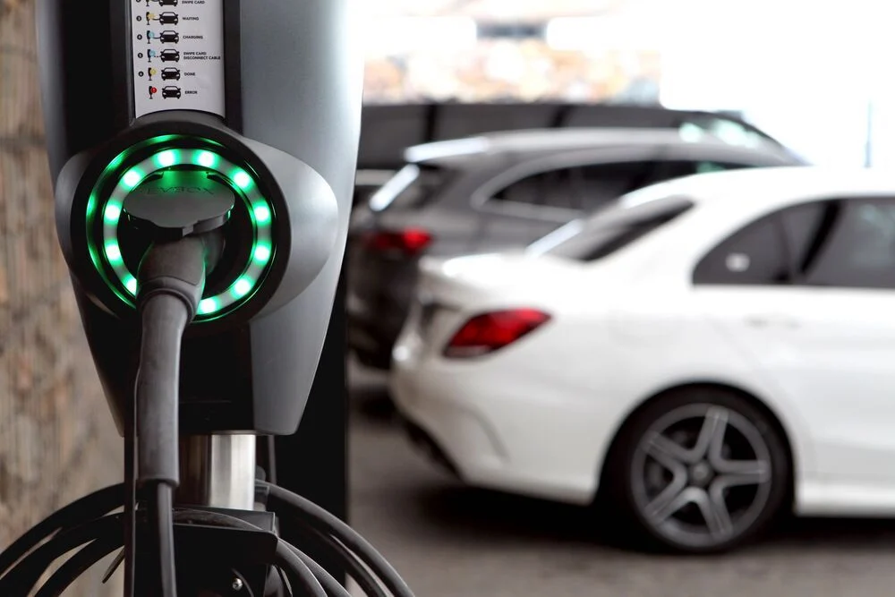 Estación de carga para vehículo eléctrico encendida con coches aparcados en el fondo.