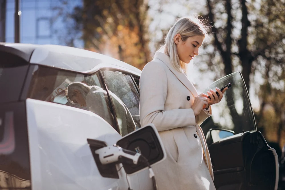 Femme près de son véhicule électrique chargeant à une borne de rechargement 
