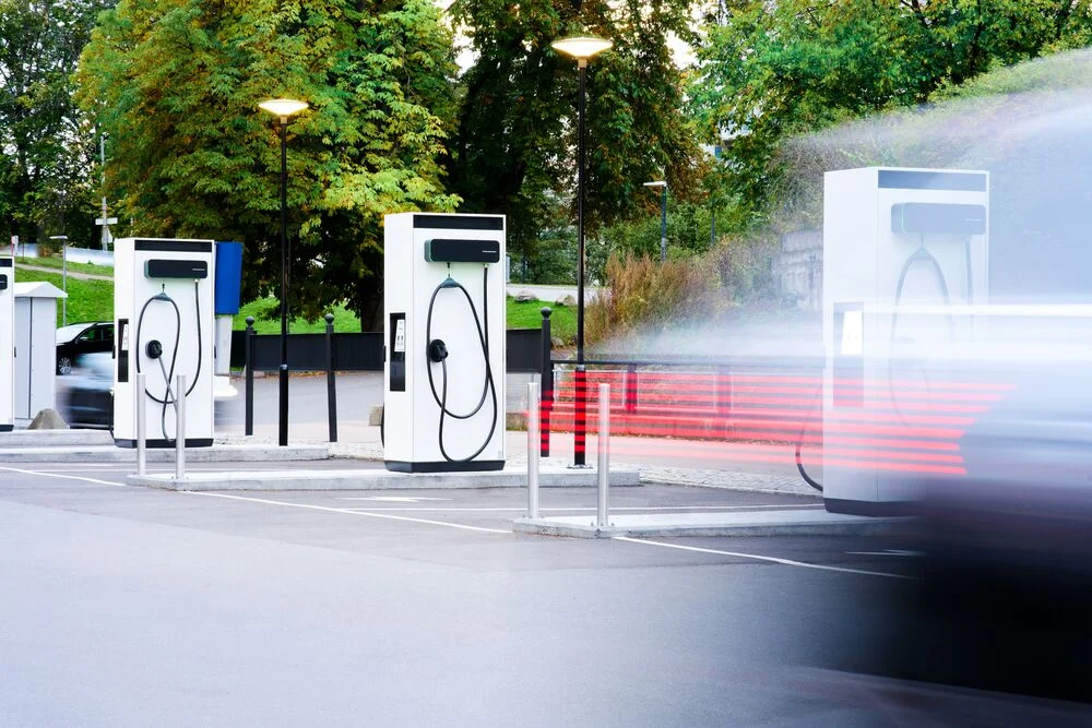 a car driving away quickly in a blurred motion in front of a parking area filled with evbox troniq modular dc fast chargers