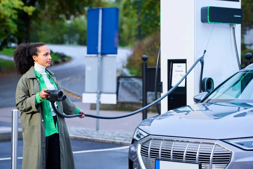 Femme branchant une voiture électrique à une borne de recharge rapide.