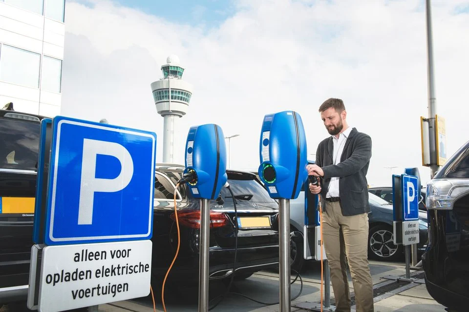 Mann lädt sein Elektrofahrzeug an einer öffentlichen Ladestation auf einem Parkplatz auf