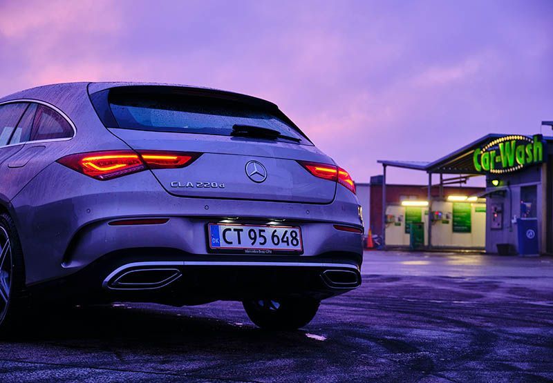 A modern car is parked front of a car wash with its headlight on in the evening.