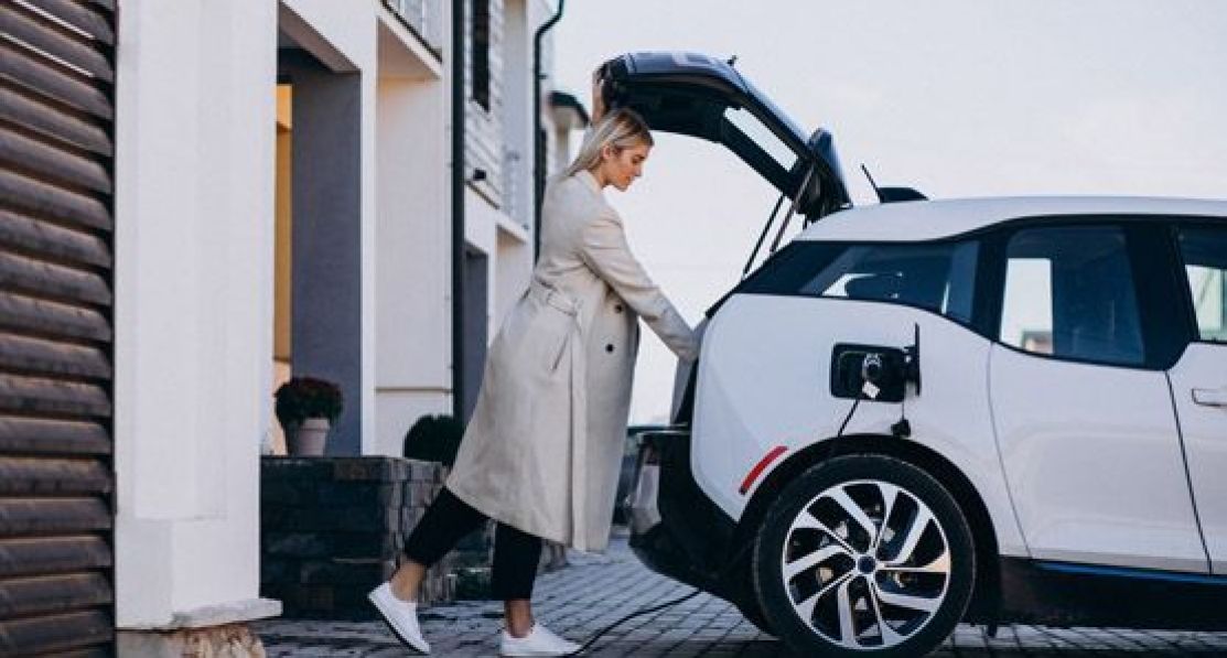 Frau belädt den Kofferraum eines Elektroautos, während es aufgeladen wird