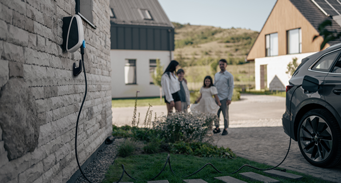 A car charging in a driveway with a family standing in the background