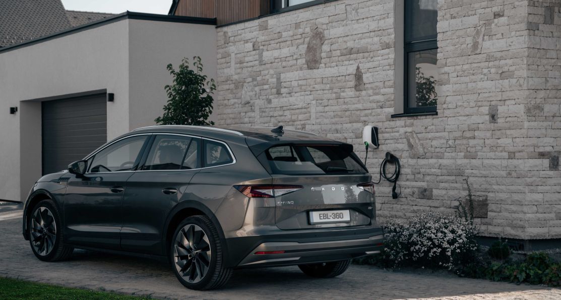 An electric SUV parked in the driveway in front of the Elvi home charging station mounted on the wall.