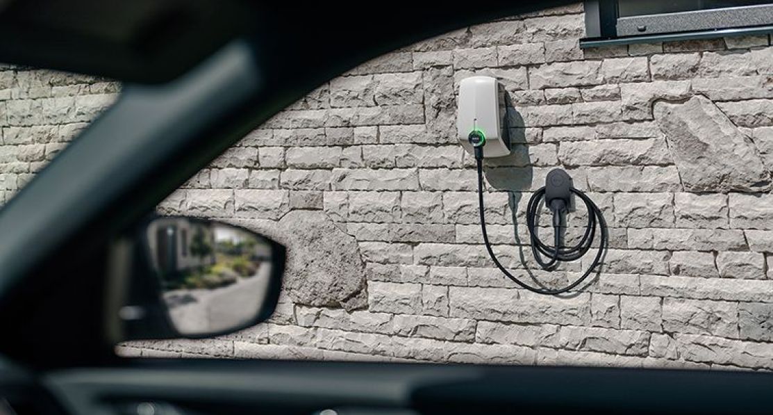 An Elvi home charging station mounted on the wall is seen by the window of the electric car.