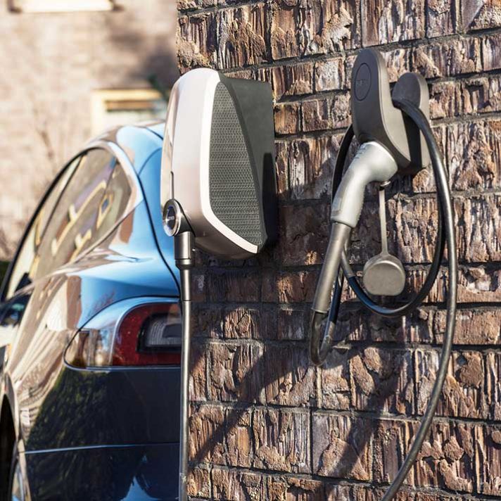 Een elektrische auto staat geparkeerd voor een huis met een EVBox Elvi-laadpaal aan de zijkant van een muur