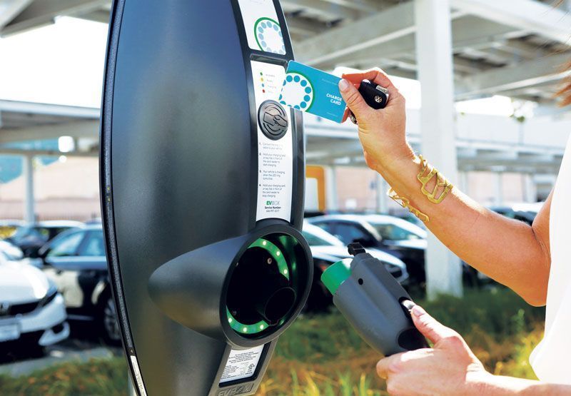 A woman swiping her card at an EVBox Business Line EV charging station with one hand, while she holds the charging cable in her other hand.