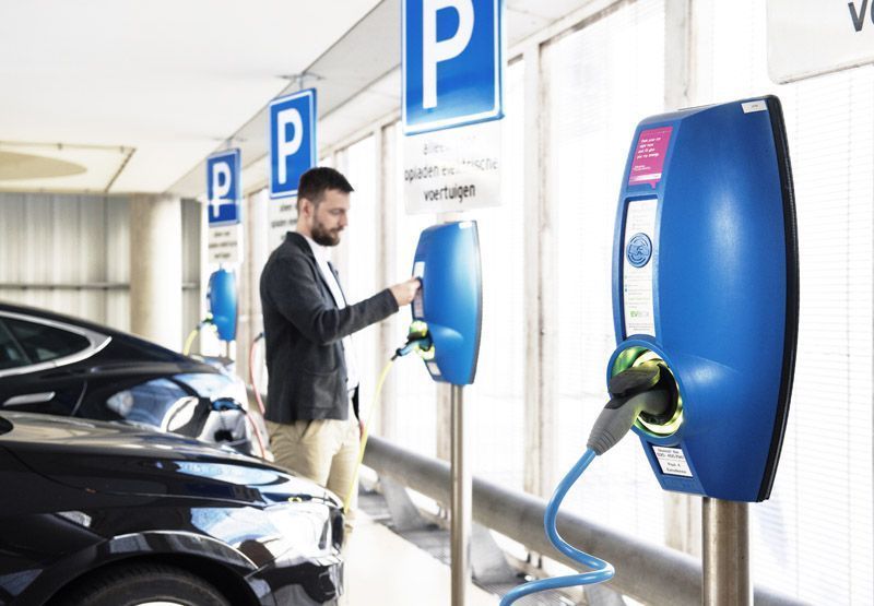 Multiple EVBox Business Line EV charging stations in a commercial parking lot. A modern man with a beard swipes a token to start a public charging session.
