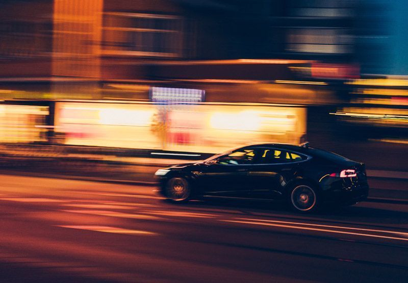 An electric car driving in an urban area at night, the image of the car is clear but the city is blurry indicating a sense of speed.