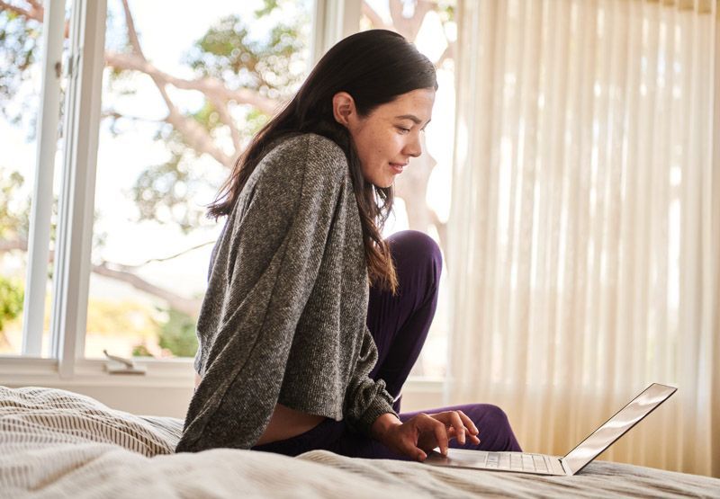 lachende vrouw op bed in slaapkamer met laptop