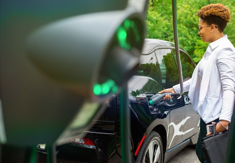 En kvinne som har på seg uformelt forretningsantrekk som kobler en EVBox Business Line-lader til det elektriske kjøretøyet sitt