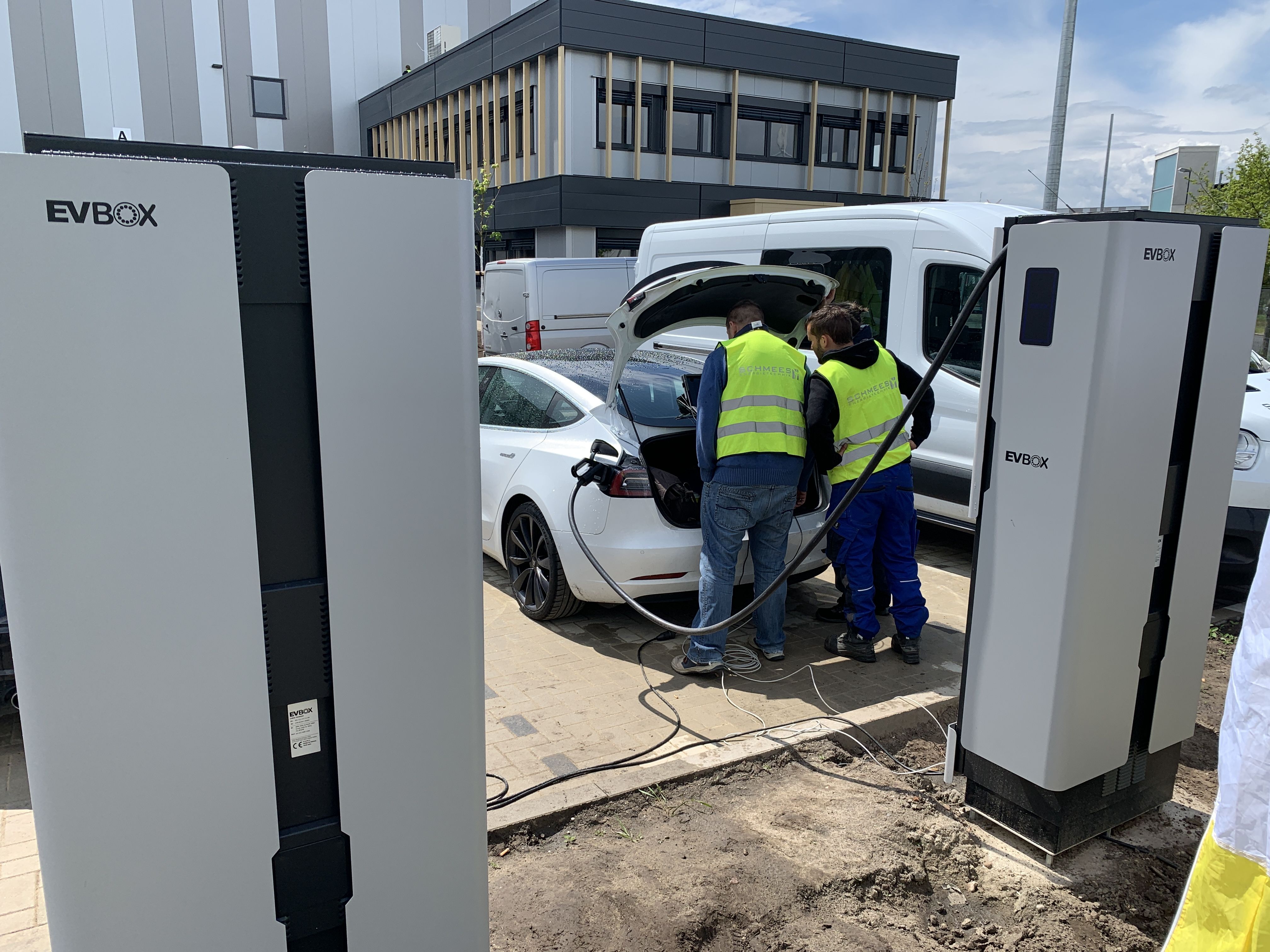 Zwei Installateure testen die neu installierten Ladesäulen für Elektroautos auf dem Firmengelände.