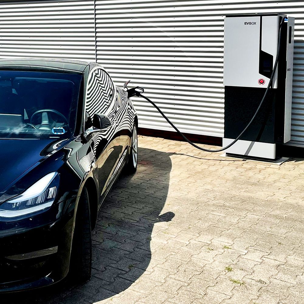 Eine Schnellladestation des Herstellers EVBox lädt ein schwarzes Elektroauto auf.
