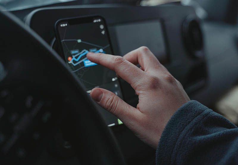 A person in a car, clicking on a smartphone that is giving directions to what could be the nearest EV charging station.