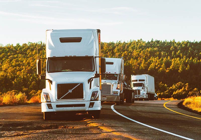 Tre tunga lastbilar parkerade längs en landsväg i solnedgången.