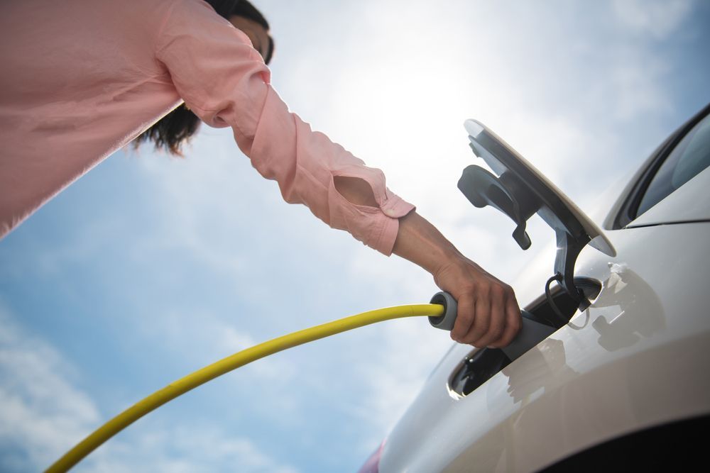 A closeup of a woman plugging in and charging her electric car on a sunny day.