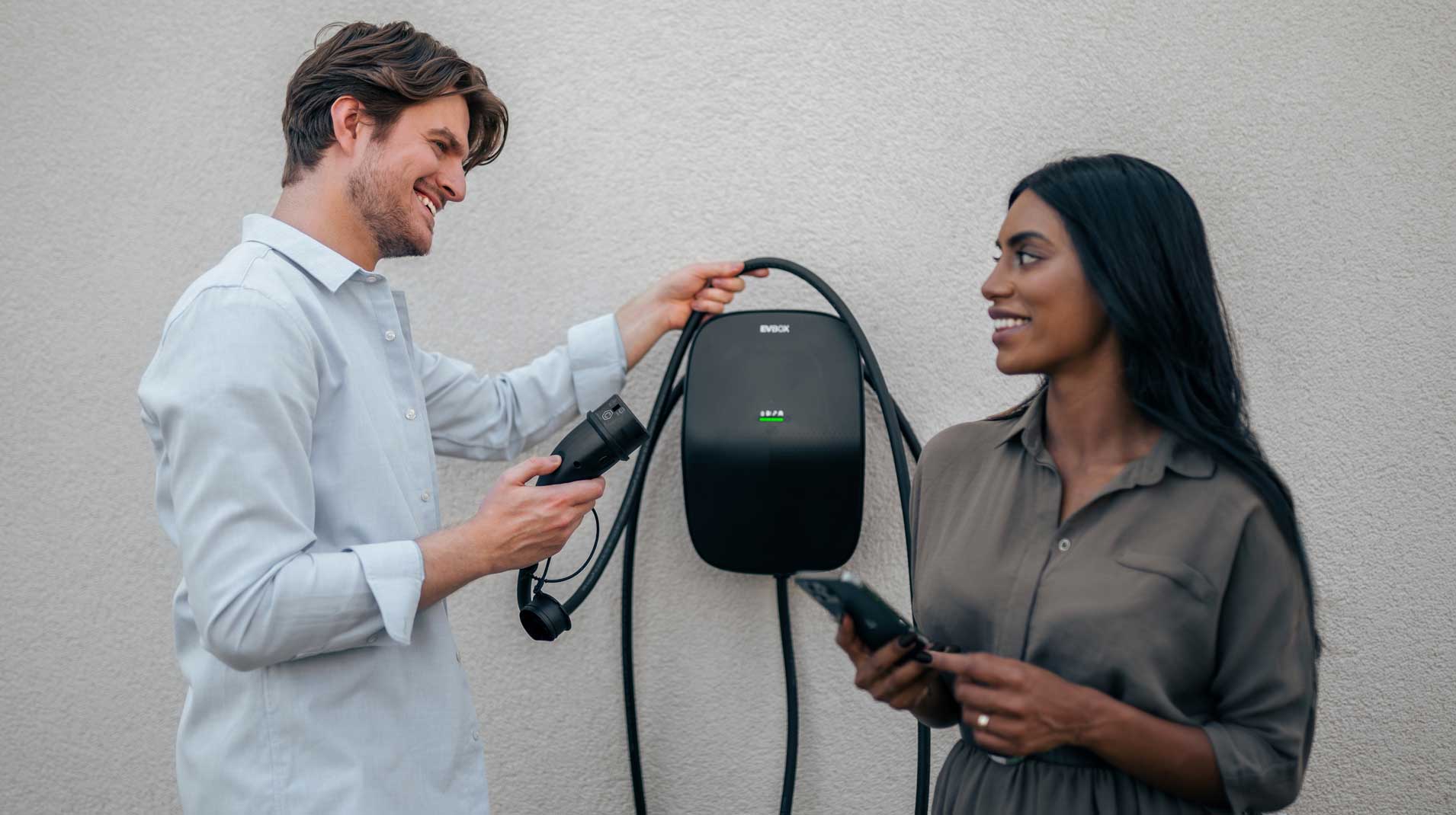 A man and a woman standing and smiling at each other in front of an EVBox Livo cable charger.