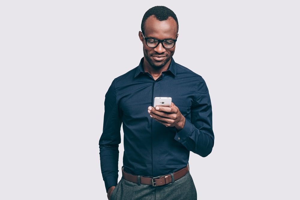 A smiling man wearing glasses looking at his smart phone to check his charging status of his vehicle.