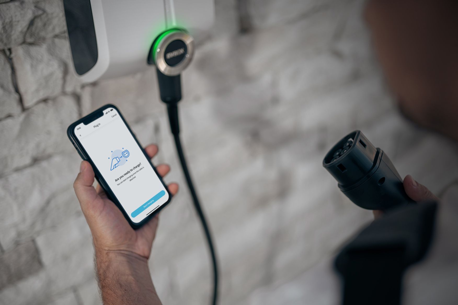 The owner of the EVBox Elvi charging station is looking at his phone that is open to the smart charger app that is asking him if he is ready to start using his EVBox Elvi charger.