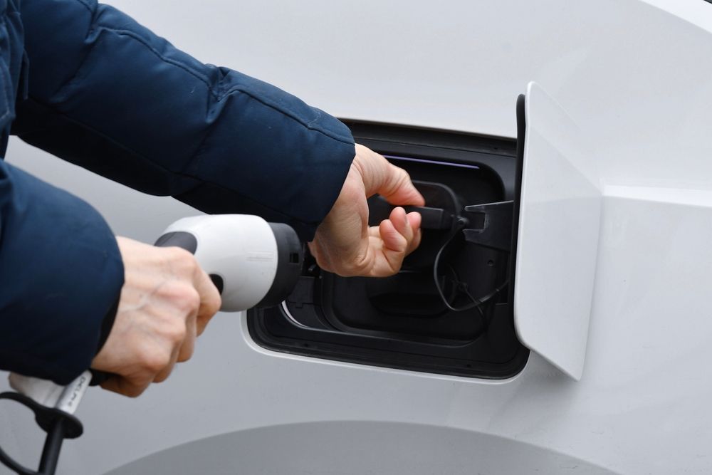 A man is opening his electric car's charger port with his left hand while holding the EV charging cable with his right hand