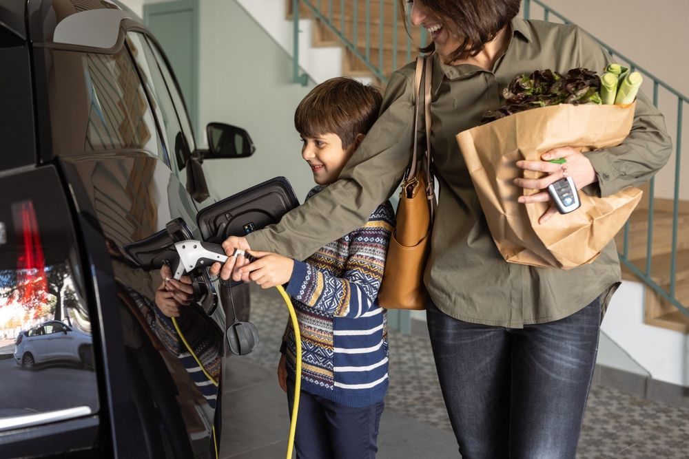 A mom and her son, connecting the charging cable to her EV with the help of her enthusiastic son.