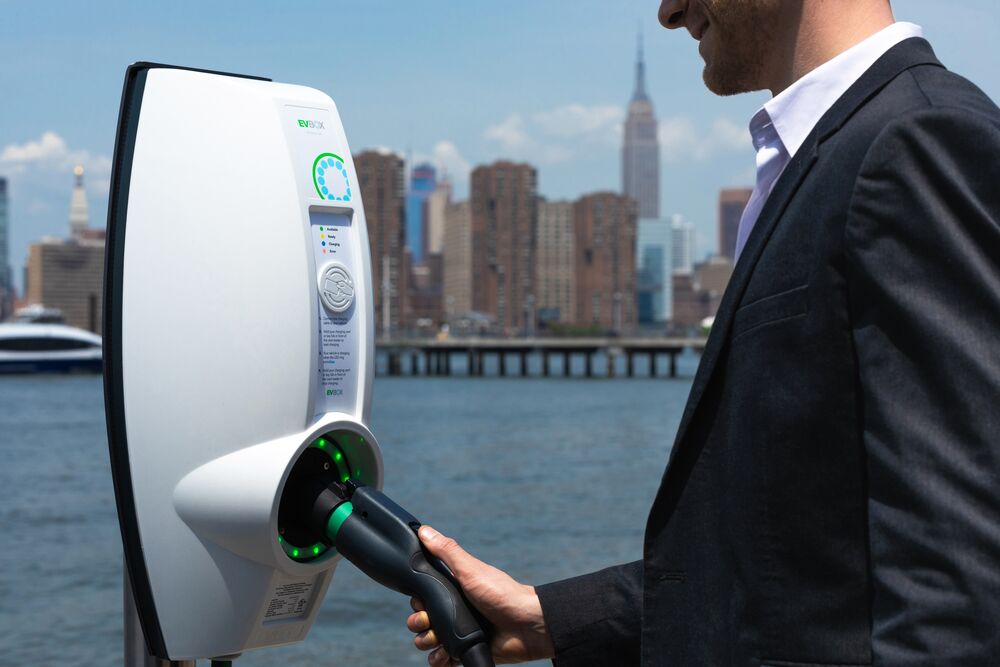 Alt: Man in suit using EVBox BusinessLine charging station with New York City skyline behind.