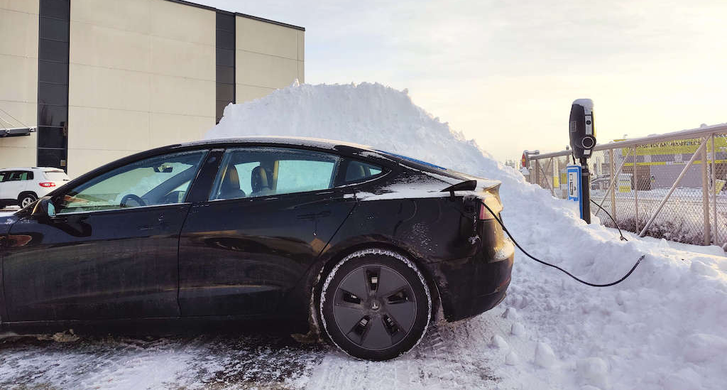 En Tesla lades ved en EVBox BusinessLine AC-ladestasjon i snøen i et industrielt miljø.