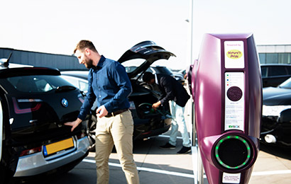 Een man sluit de kofferbak van zijn elektrische auto naast een EVBox BusinessLine laadstation.