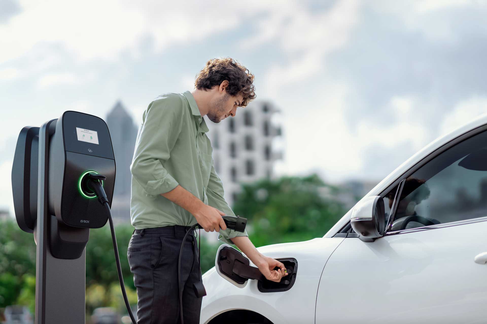 A man using a public EVBox Liviqo AC charging station to charge his electric car.