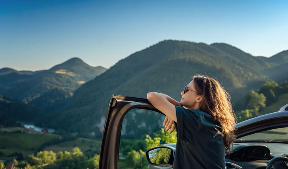 A woman is looking at the mountains while standing besides her EV.