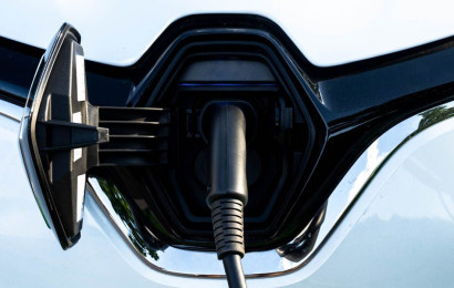 Close-up of white electric car charging port with charging plug inserted.