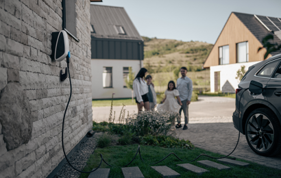 A car charging in a driveway with a family standing in the background