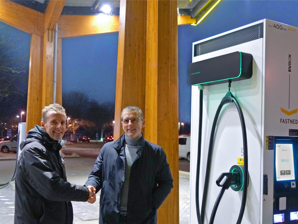 EVBox- og Fastned-medarbejdere giver hånd ved siden af en EVBox Troniq High Power-ladestation.