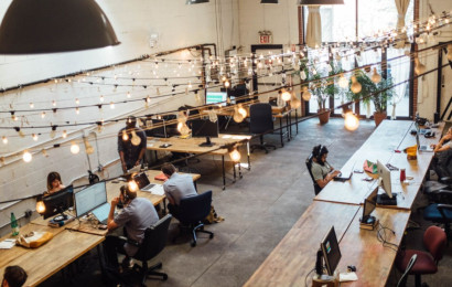 A little-lit modern workplace with young professionals spread across multiple desks.