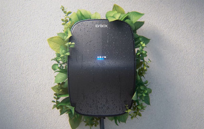 An EVBox station attached to a wall with green branches growing out of it from the back