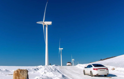 En Tesla som kjører gjennom et vinterlandskap med store vindmøller på siden av den snødekte veien
