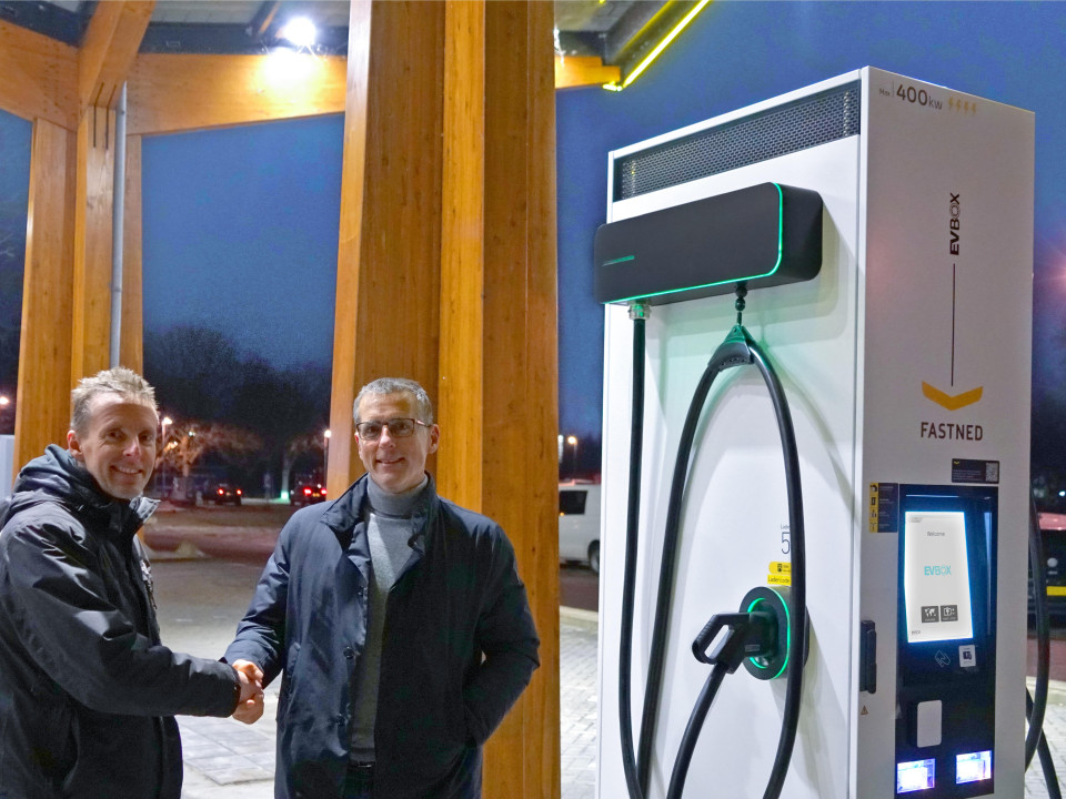 Empleados de EVBox y Fastned se dan la mano junto a una estación de carga EVBox Troniq High Power