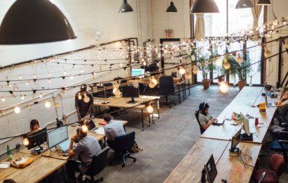 A little-lit modern workplace with young professionals spread across multiple desks.