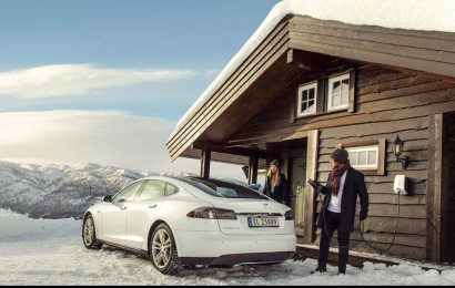 En mann som lader Tesla-elbilen sin med EVBox Elvi-ladestasjon på en hytte om vinteren