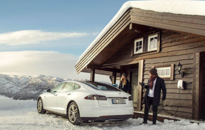 In the mountains, a man connects his car to the charging station while standing in the snow.
