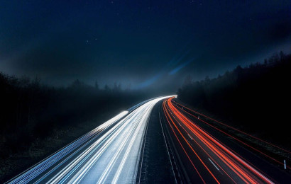 Een snelweg midden in het bos, laat in de avond, met lichtstralen op de achtergrond die de snelheid weergeeft van de auto’s
