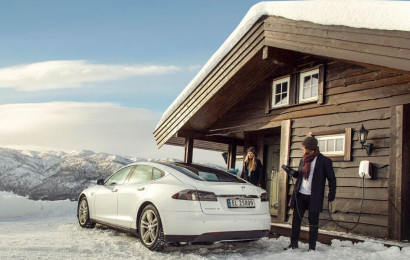 En mann lader en Tesla med en EVBox Elvi-ladestasjon på en hytte om vinteren