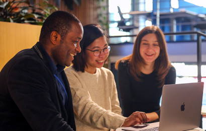 Un homme et deux femmes regardent un ordinateur portable au milieu d'eux, ils sourient tous à l'ordinateur.