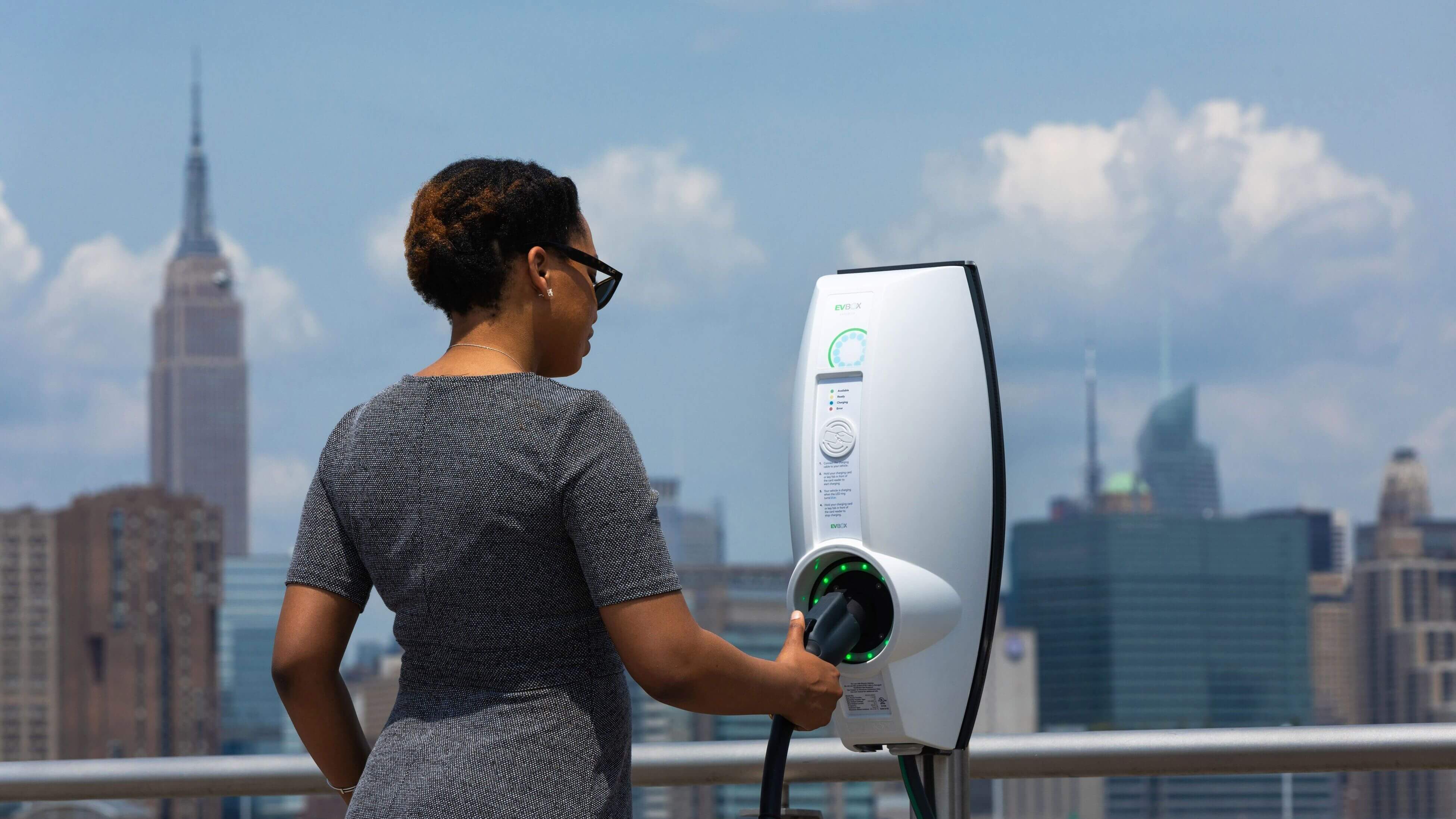 A woman charging using a white EVBox BusinessLine with the New York skyline in the background